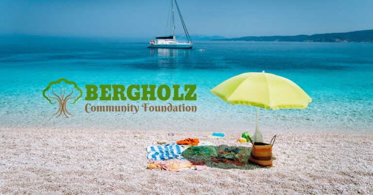 Beach scene with a boat on the water and a beach umbrella and accessories set up with the Bergholz Community Foundation logo