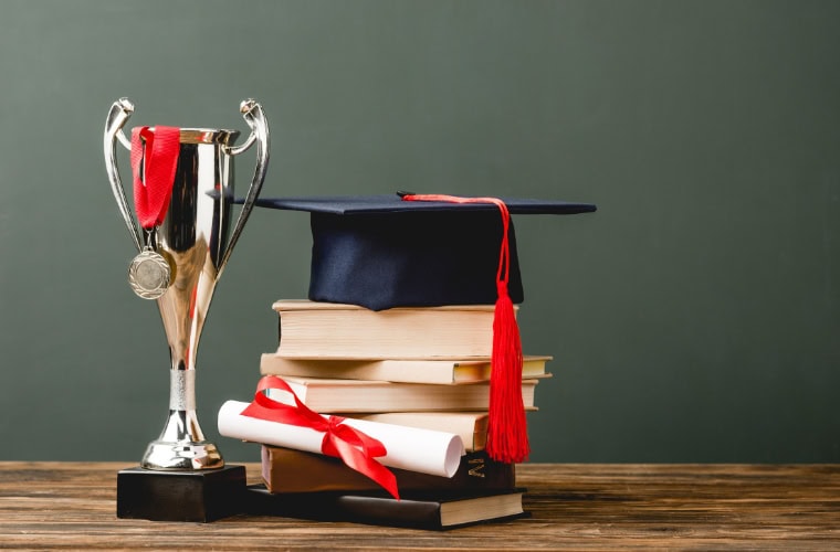 A graduation cap, diploma and stack of books