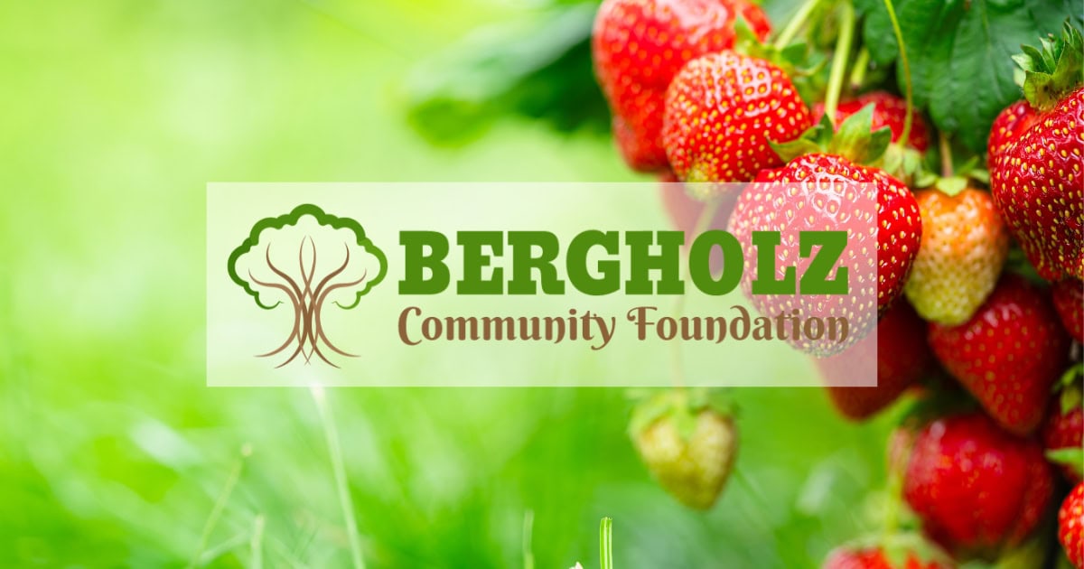 Up close image of bright red strawberries hanging from a plant with the Bergholz Community Foundation logo centered over the image.